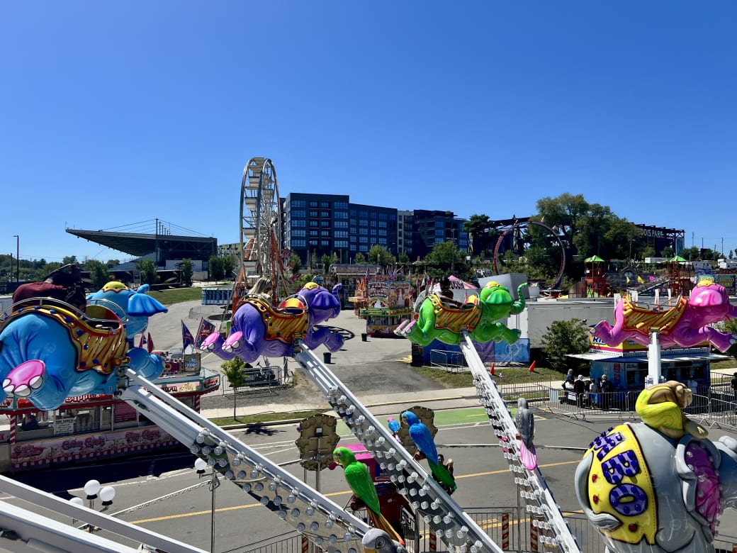 A fair ride with flying elephants. Below there are fair food food trucks, a Ferris wheel, and roller coasters.