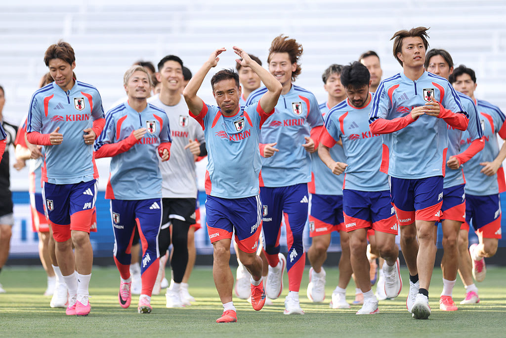 The Japanese men's football team run across the soccer field in light blue jerseys and darker blue shorts.