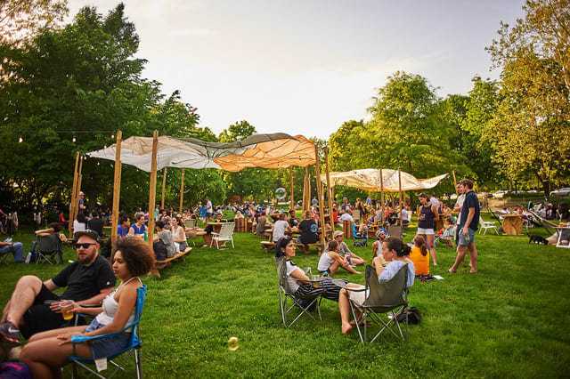 People lounging on chairs and under tarps in a park.