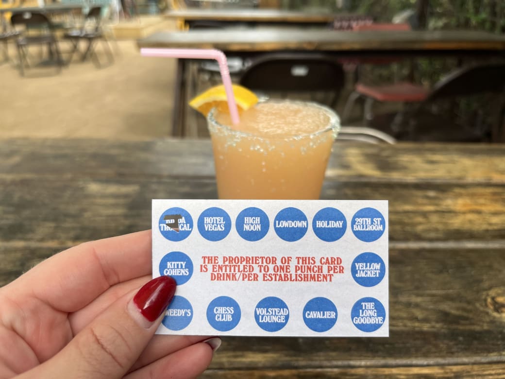 A person holding a punch card with blue dots on it in front of a light orange frozen drink.