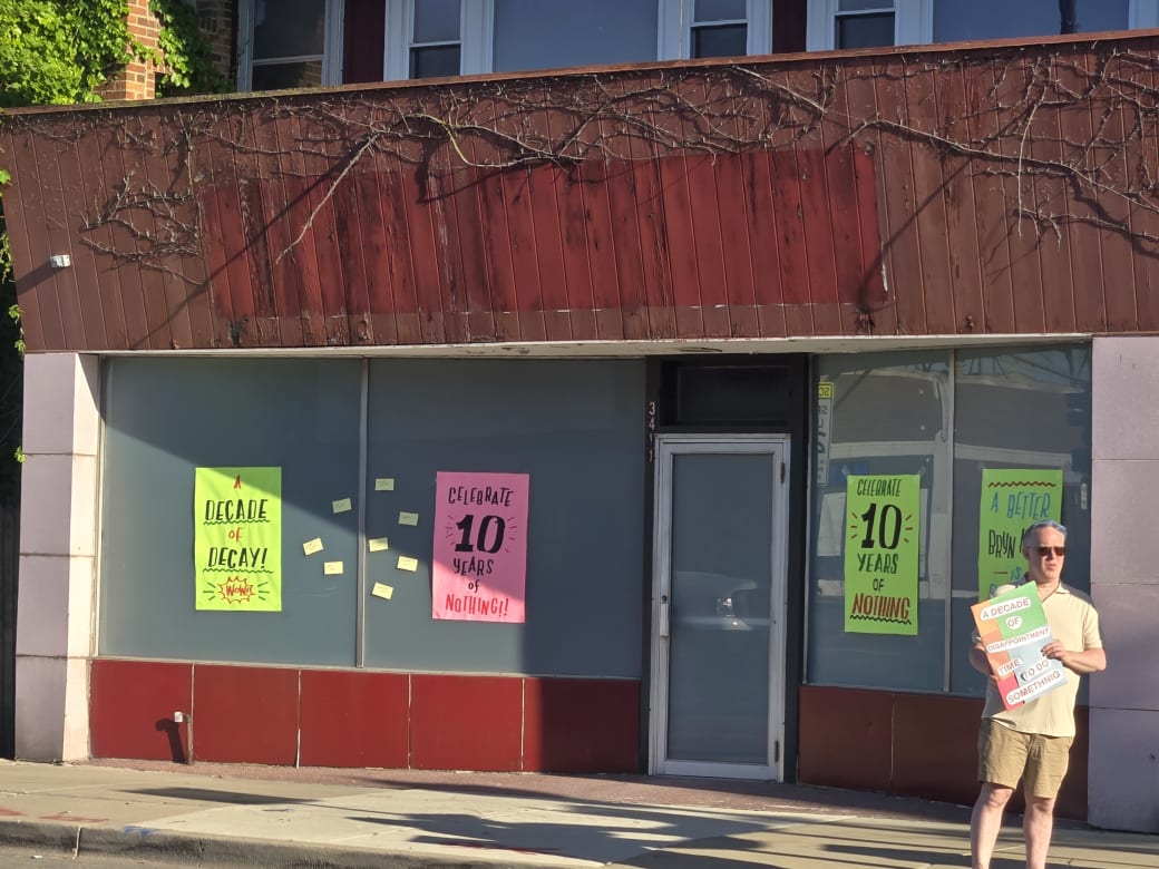 The outside of a building that closed down. There are signs on the window that say "decade of decay" and "Celebrate 10 years of nothing"