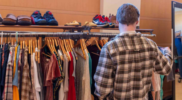 A man in a plaid shirt peruses a rack of clothes.