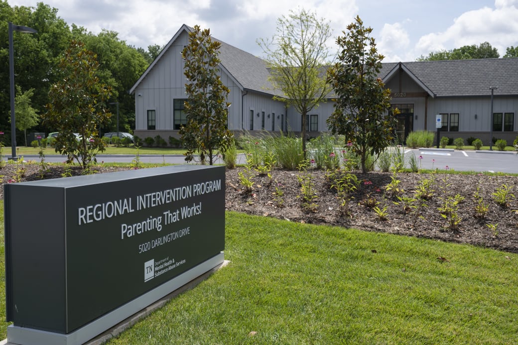 A gray building with flower beds in front of it. A gray sign says: Regional Intervention Program: Parenting That Works!