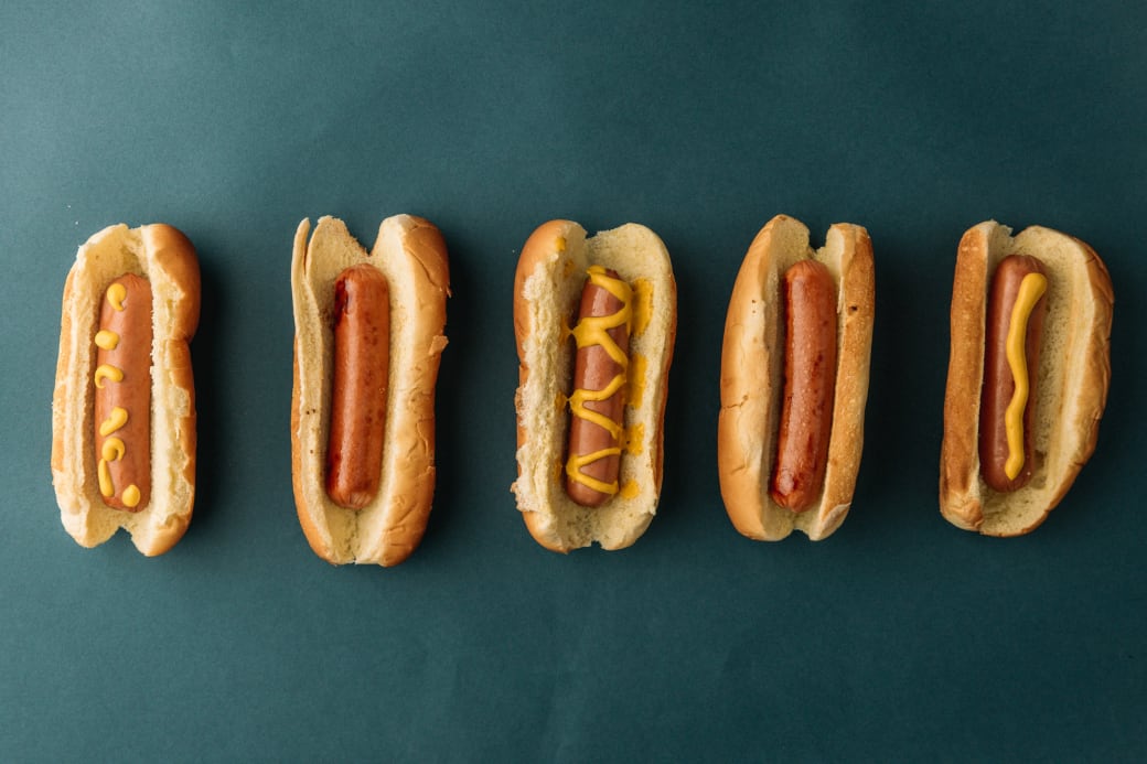 Five hot dogs, three with mustard and two without, on a blue background