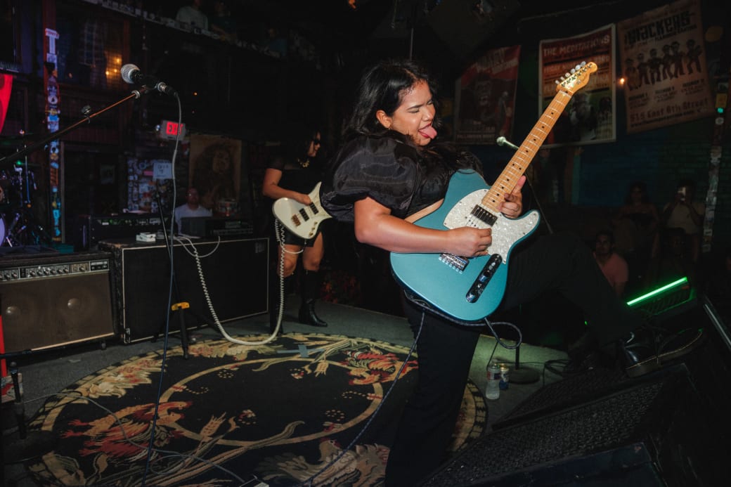 A person playing a blue guitar and sticking their tongue out.