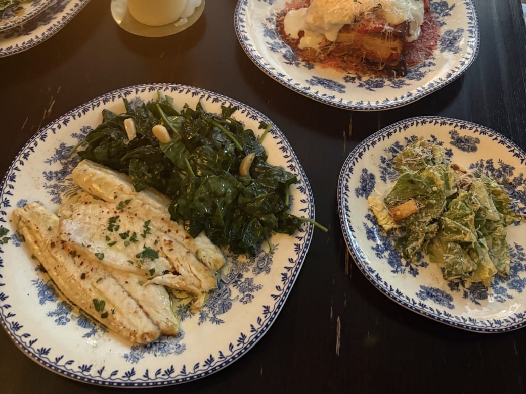 Three white porcelain plates with blue flowers on a wooden table, loaded with dinner items.