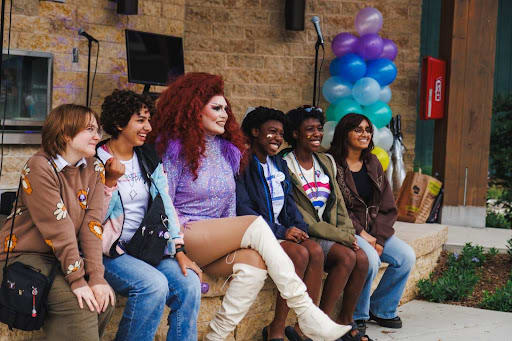 A group of 6 people sit on a bench smiling, looking on at the Middleton Pride Festival