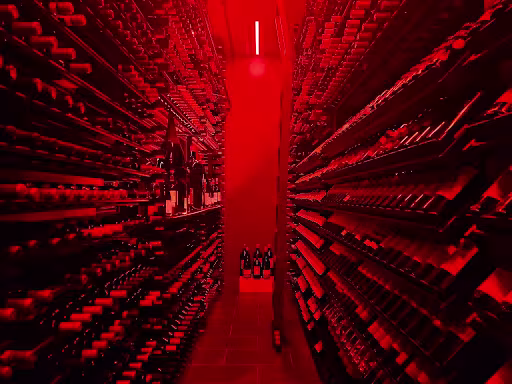 A wine cellar with bottles along the wallis shown in a red light.
