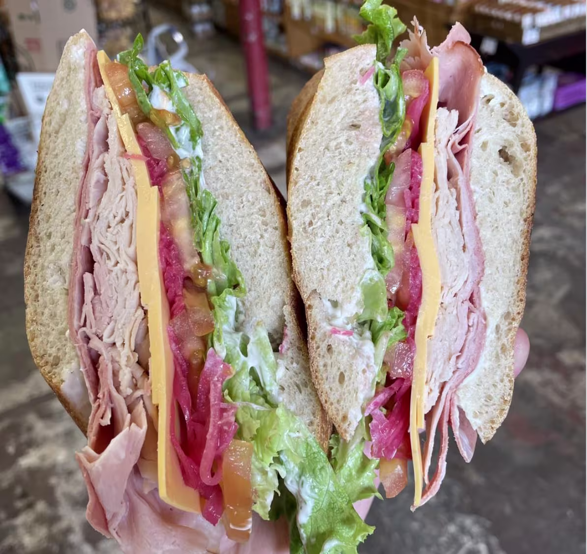 A person holds open a sandwich with deli meat and cheese and tomatoes