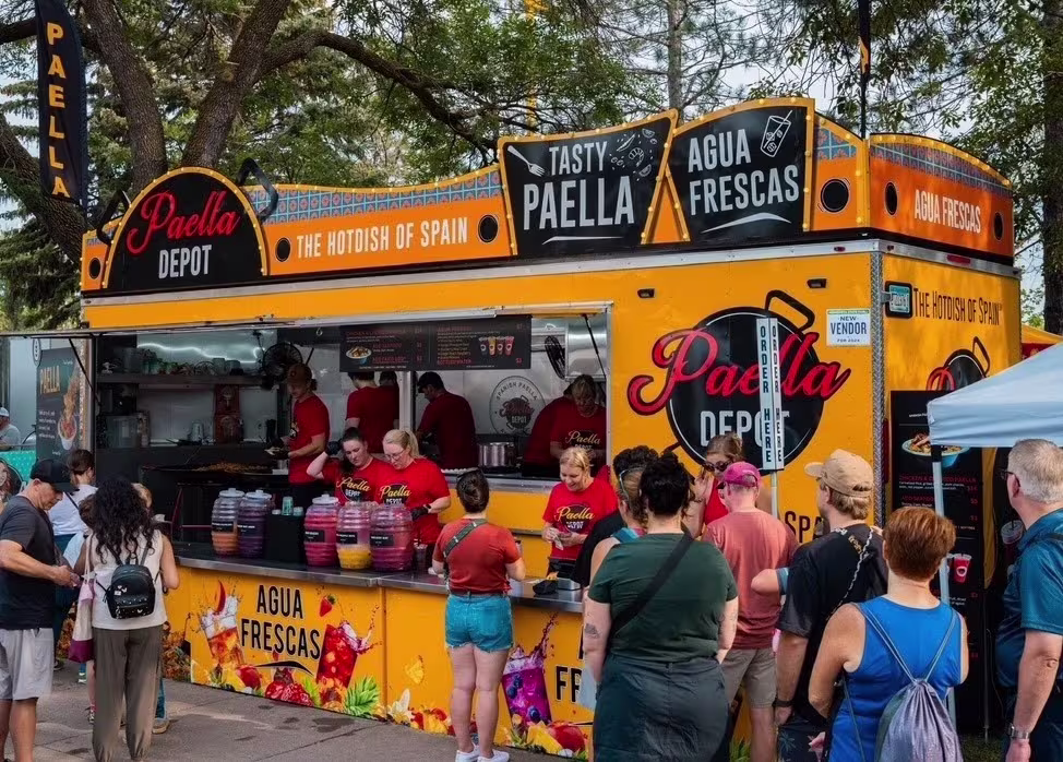 People gather around food stand with signage that reads, "Paella Depot"