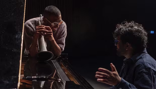 A man with a brass instrument speaking to a man at a piano