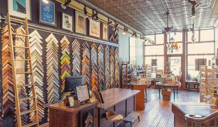 The interior of Mitrebox Framing & Gifts, with hundreds of triangular wood frame pieces mounted on the walls, and other frames and displays.