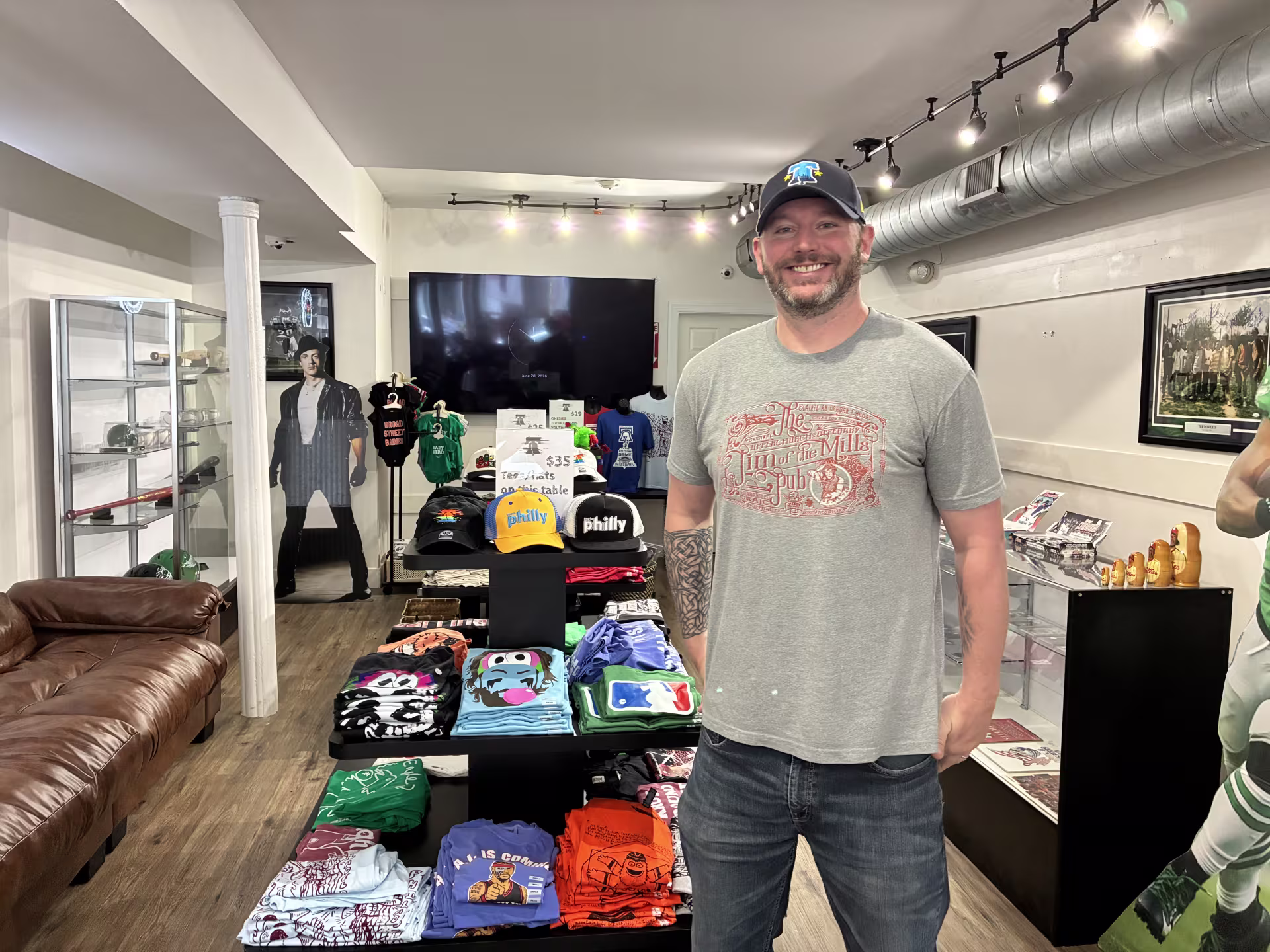 Alt text: John Foley, owner of Foley’s: The Philly Sports Shop, stands in his shop surrounded by displays of Philly sports merchandise and apparel.  