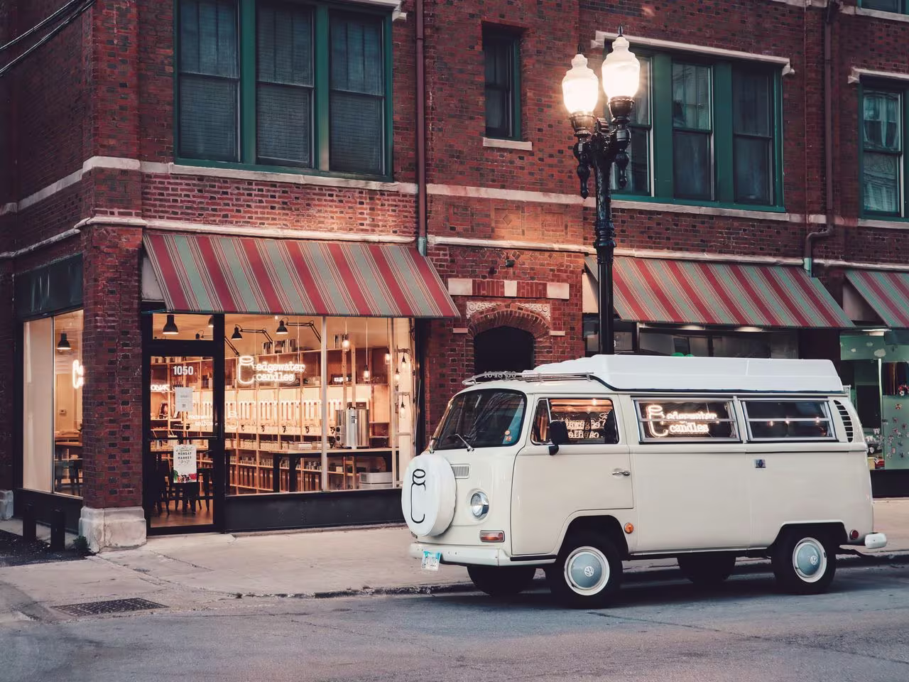 An old school VW van parked on the street in front of a lamp and brick building