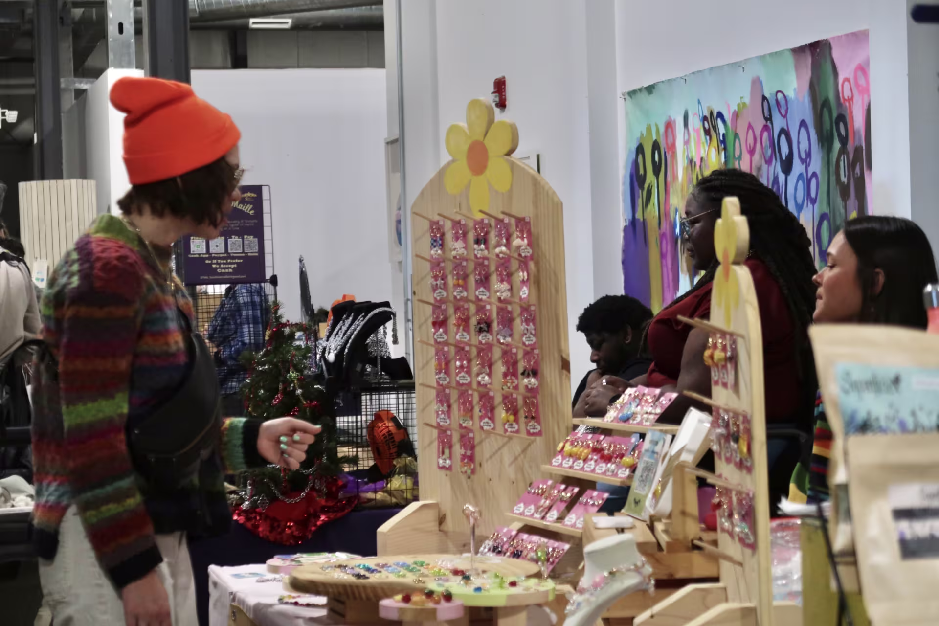 A person in an orange beanie shops at a market vendor booth.