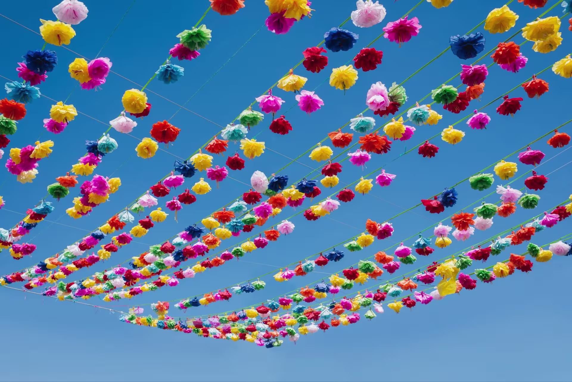 Colorful paper flowers on strings against a blue sky.