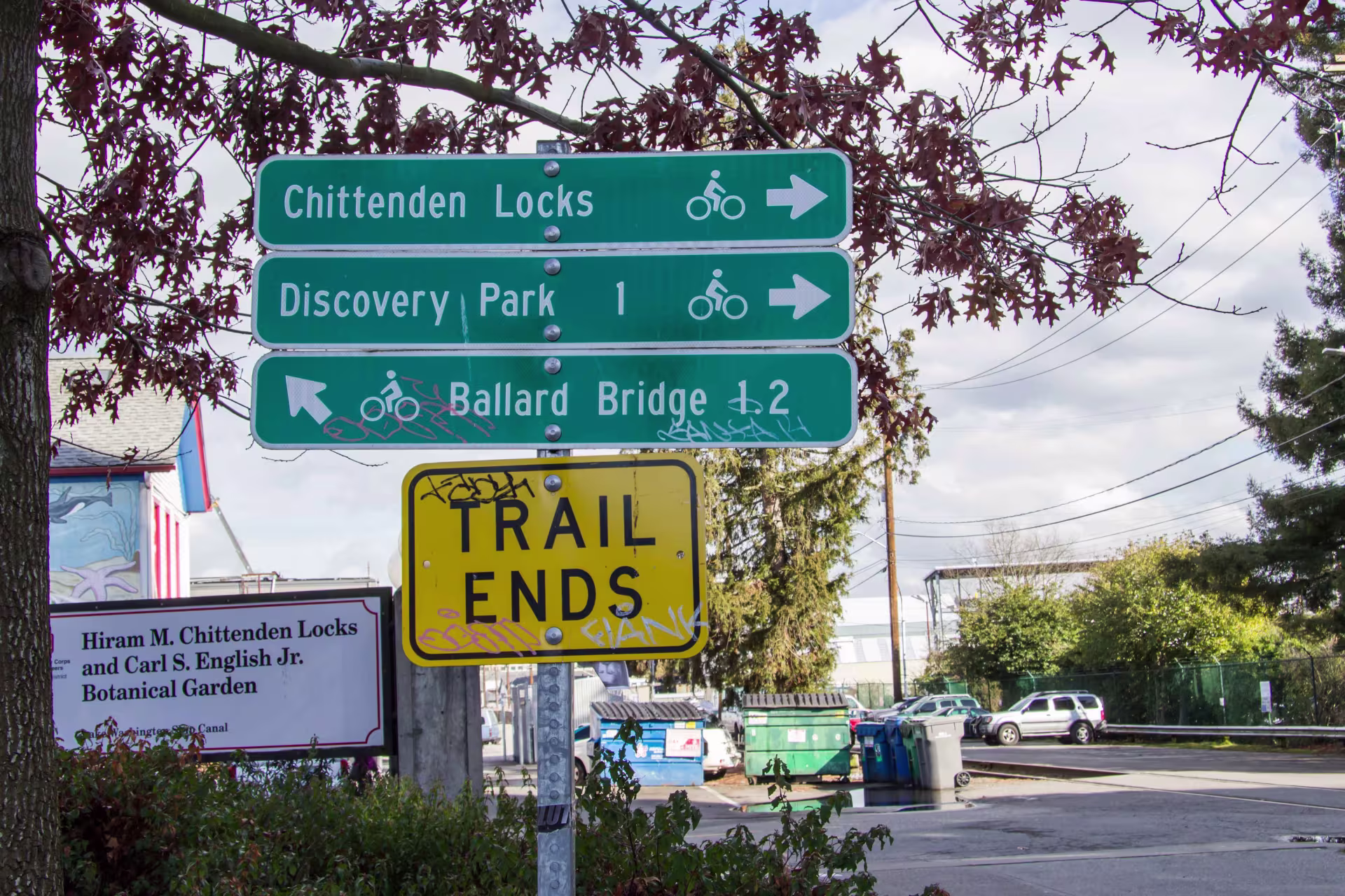 A stack of 4 signs. The top one says "chittenden locks" and points right. The one below says "discovery park" then points right. The one below that says "ballard bridge" then points diagonally up to the left. The one below that says "trail ends"
