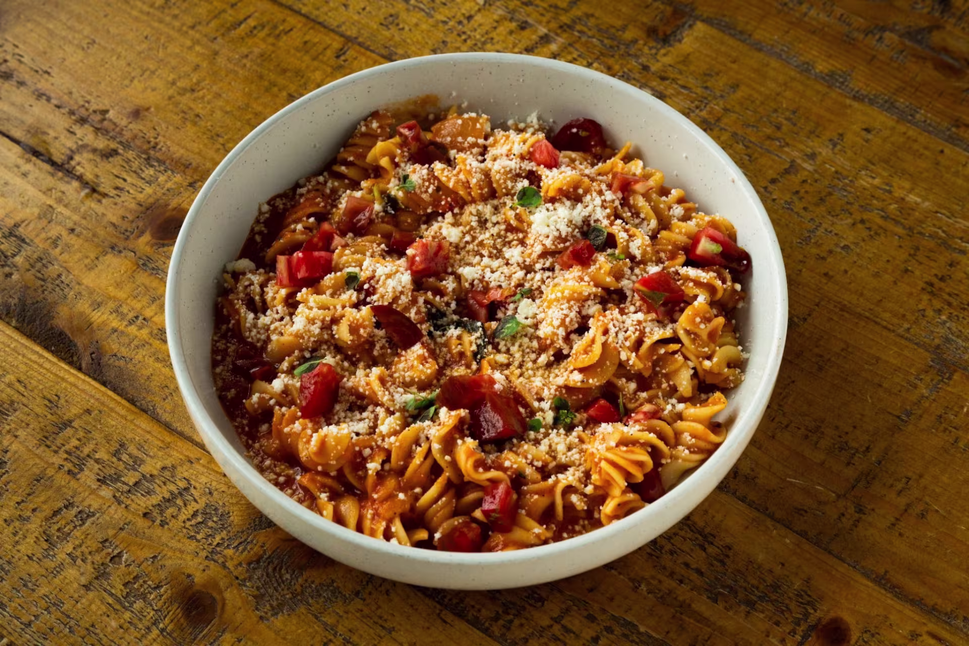 A bowl of pasta with parmesan and tomatoes and pepper