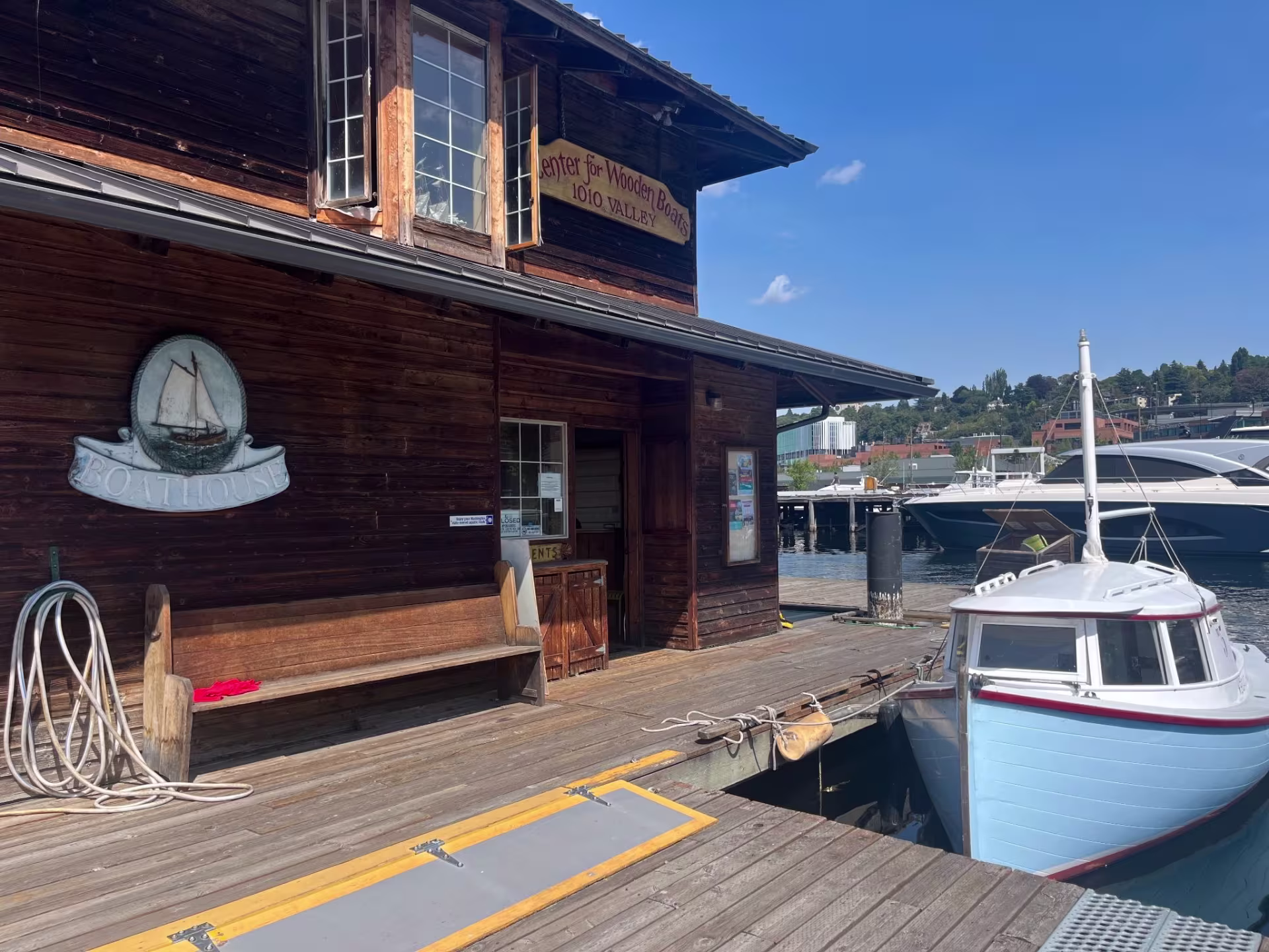 A boat docked on a pier with a shop on it. "Boathouse" is faintly written on the sign below and "Center for Wooden Boats" is written on the sign on the second floor