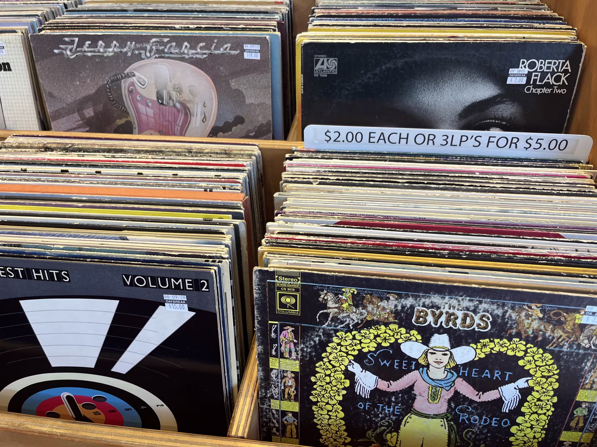 A close-up of rows of records for sale, including a Jerry Garcia album, a Roberta Flack album, and the Byrds' “Sweetheart of the Rodeo.” One of the rows of records has a sign above it reading "$2.00 EACH OR 3 LP'S FOR $5.00."
