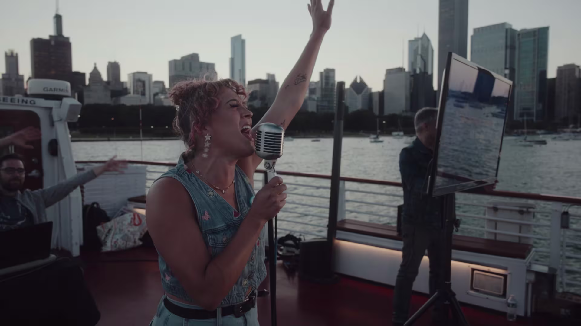 A woman singing into a mic. A man is holding up what looks to be a tv screen