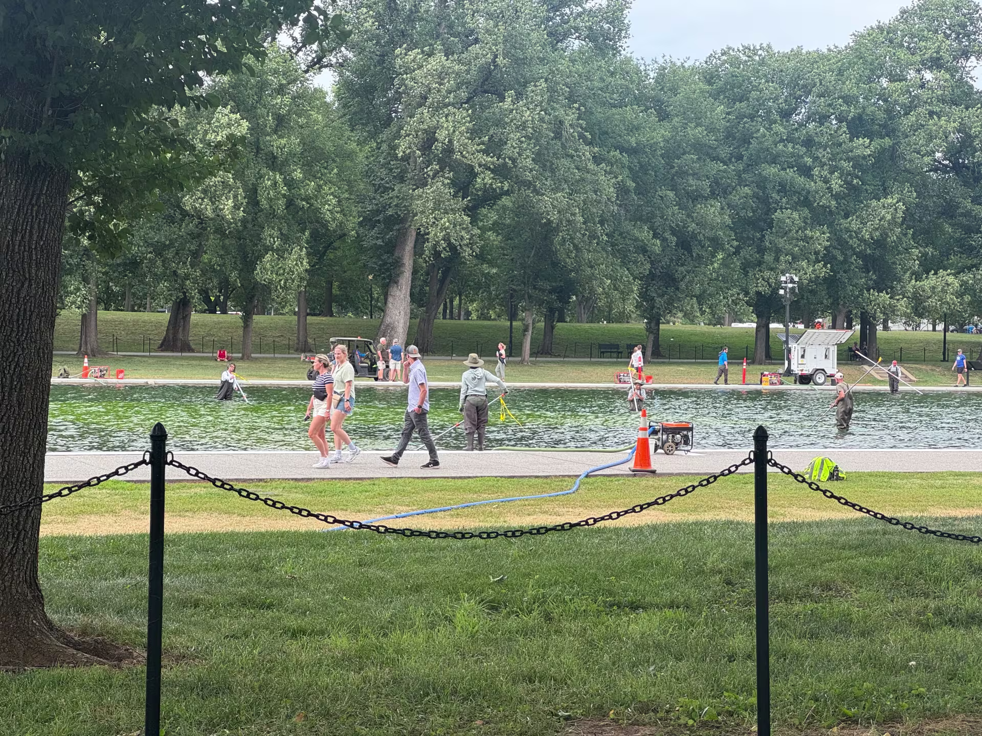 Tourists walk by as crews try to clean the algae bloom in the Reflecting Pool.