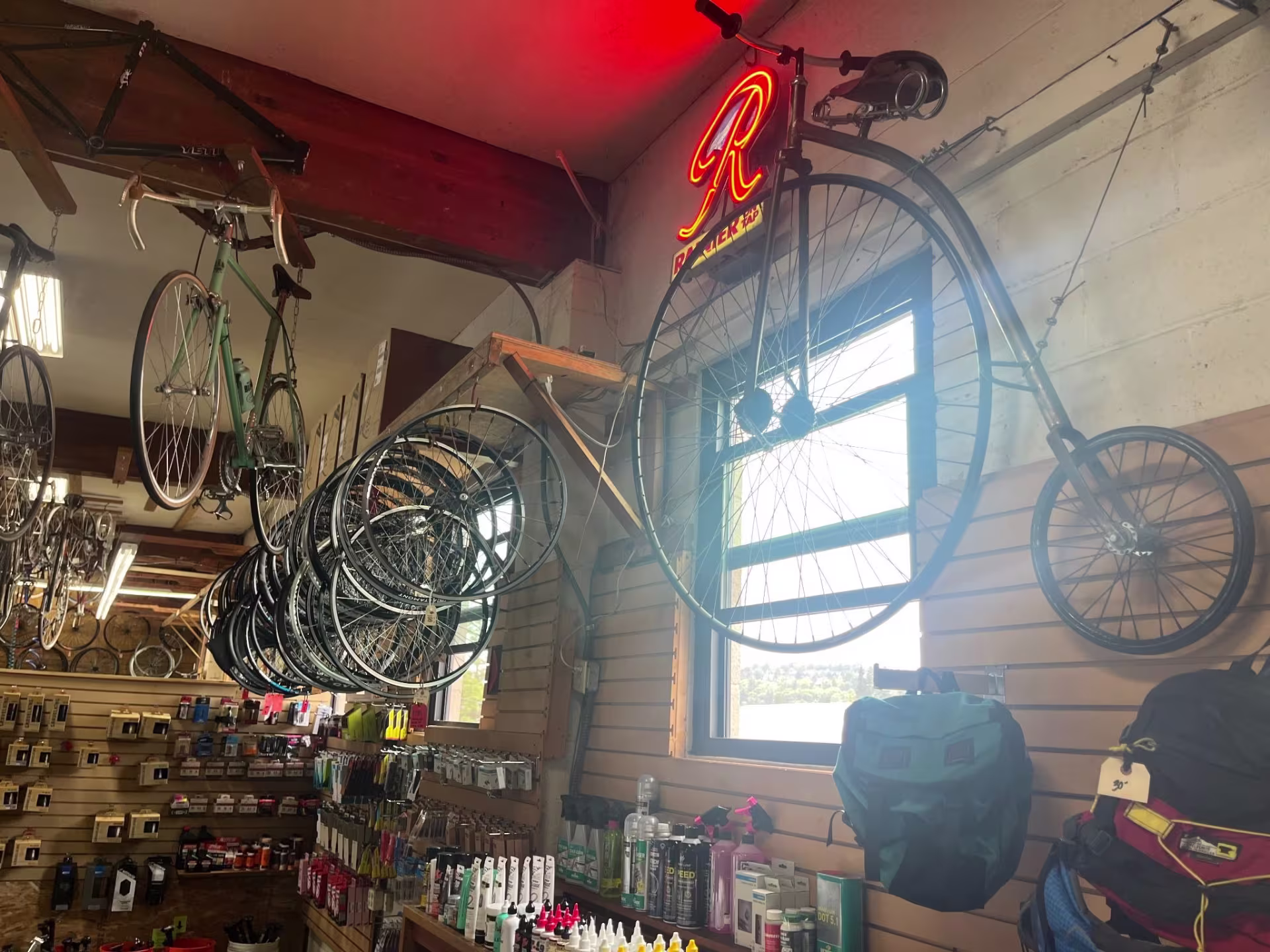 The inside of a bike shop where wheels and bikes hang on the wall. A standout bike is older looking bike where the front wheel is very big and the back wheel is very small