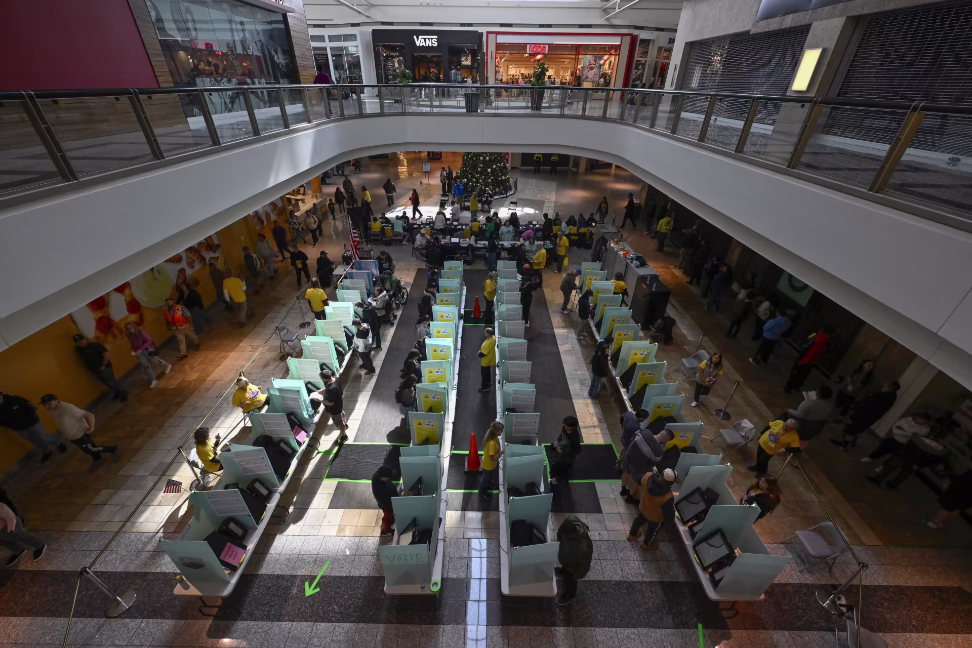Poll workers in yellow shirts look over people voting in voting booths set up at a mall.