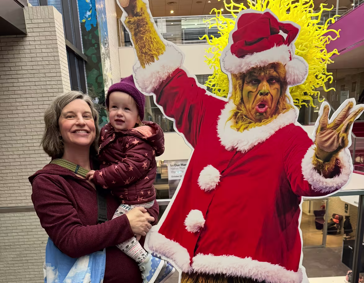 A mother and 3-year-old daughter smile next to a cardboard cutout of The Grinch at the Children’s Theater in Minneapolis, MN.