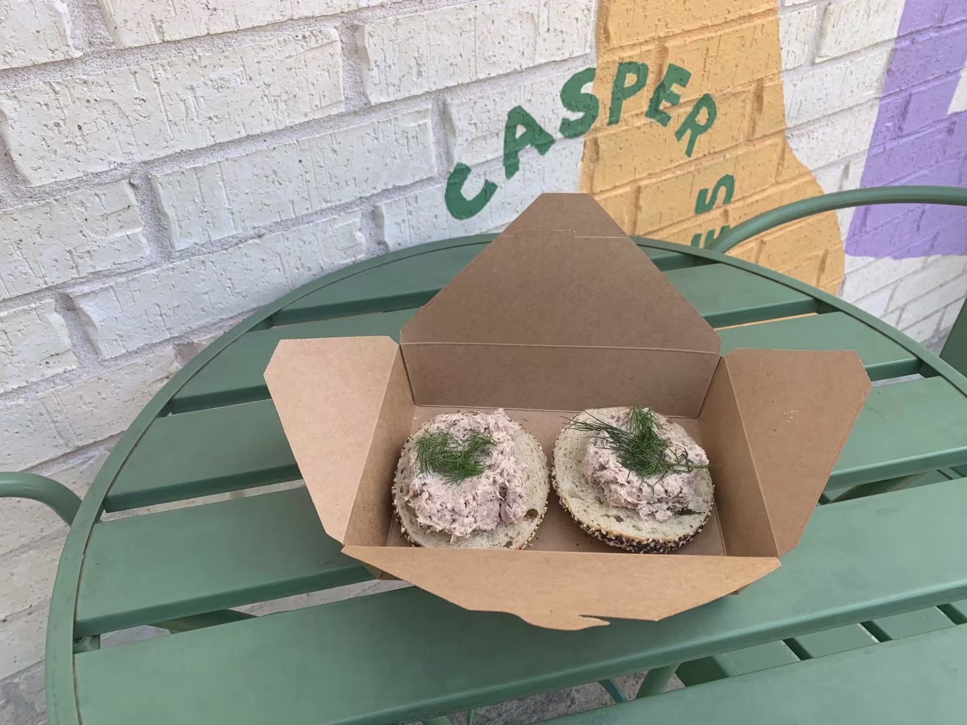 A tuna fish bagel on a green patio table.
