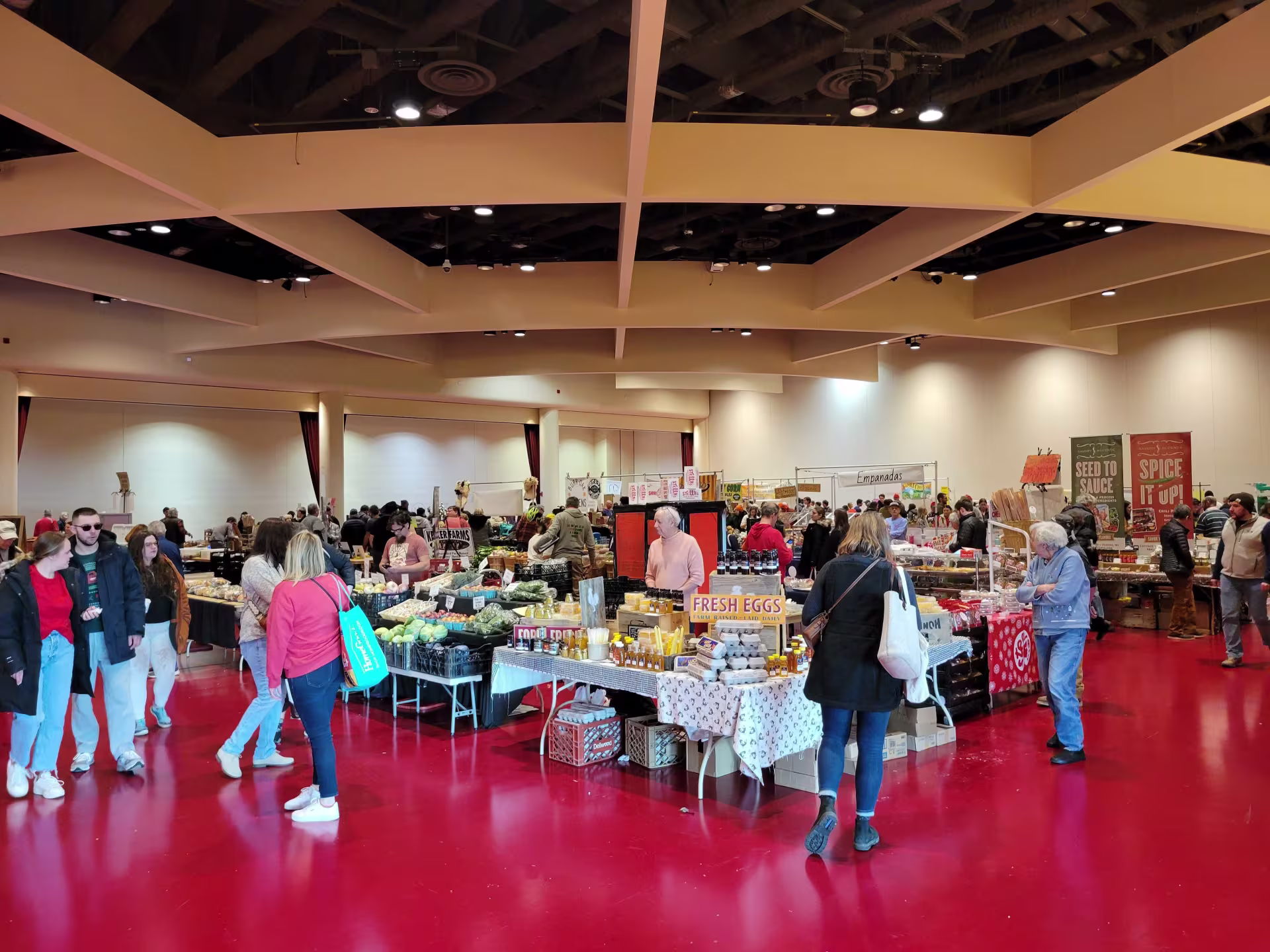 People shopping at tables in an indoor market with a red floor. 