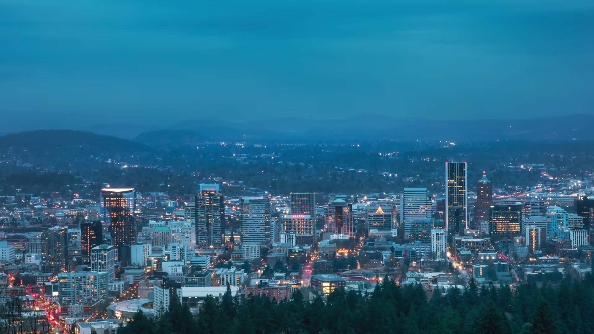 Downtown Portland’s skyline sparkles during blue hour. The perspective shows the view from Pittock Mansion, facing eastward.