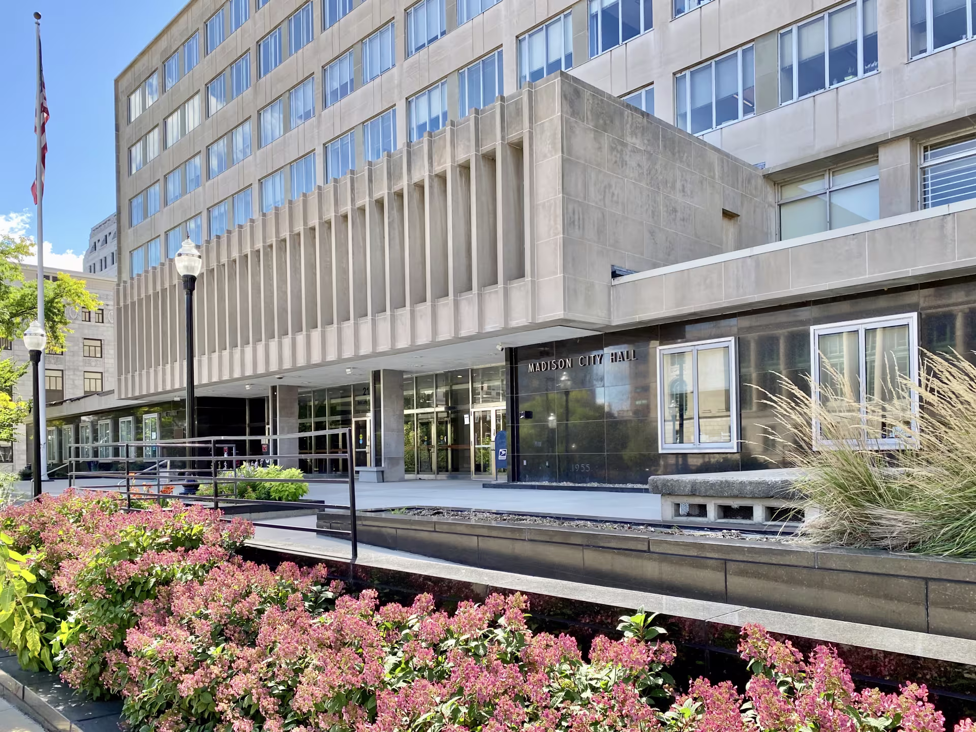 A gray government building with red flowers in front.