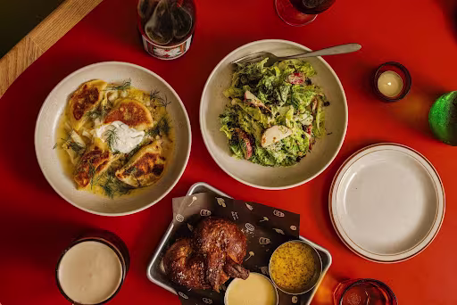 A top-down view of a spread of food on a bright red table, including pan-fried dumplings, a salad, and roasted chicken with sauces.