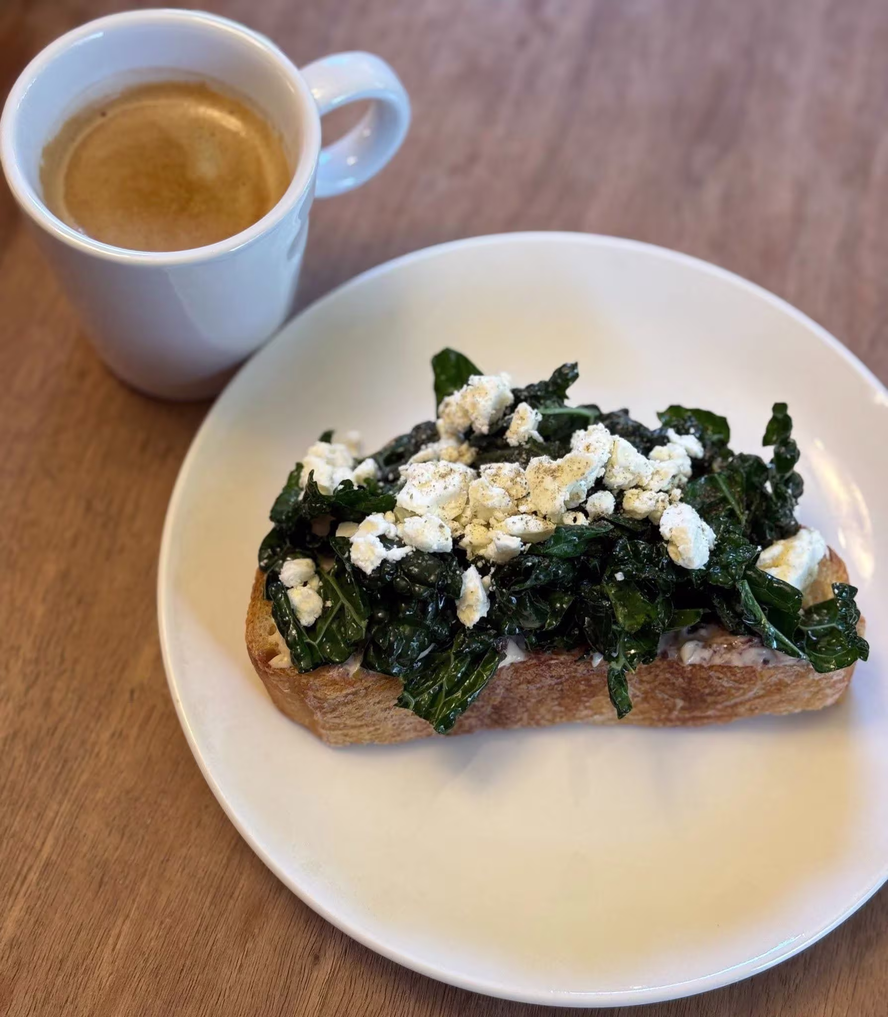 Cup of coffee and toast on a plate topped with kale and and goat cheese