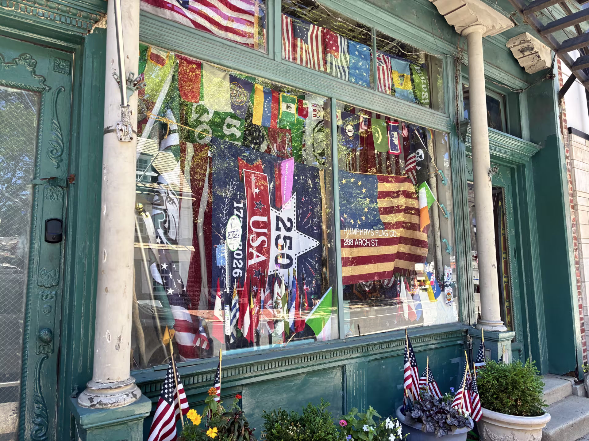 The storefront of Humphrys Flag Company with large and small flags seen through the windows. 