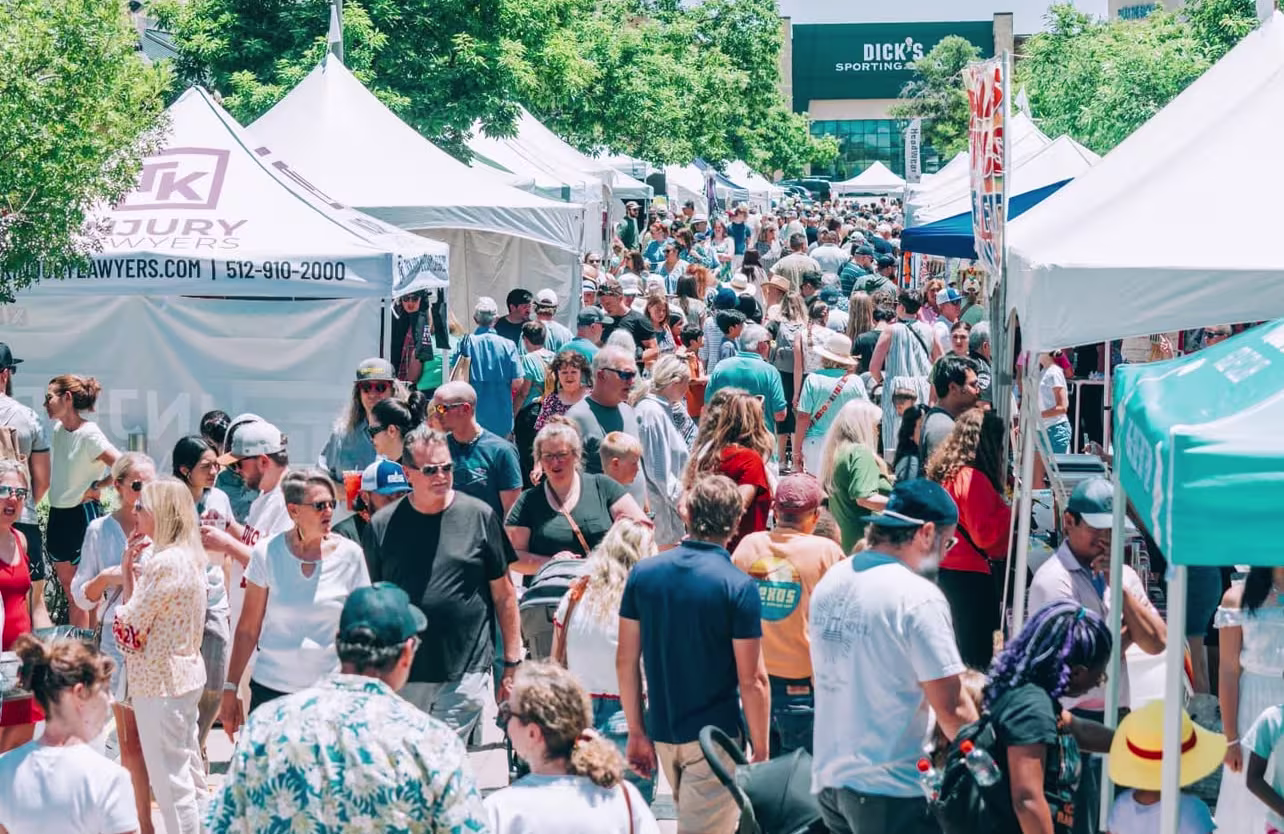 A crowd of people walk through a festival with vendor booths. 