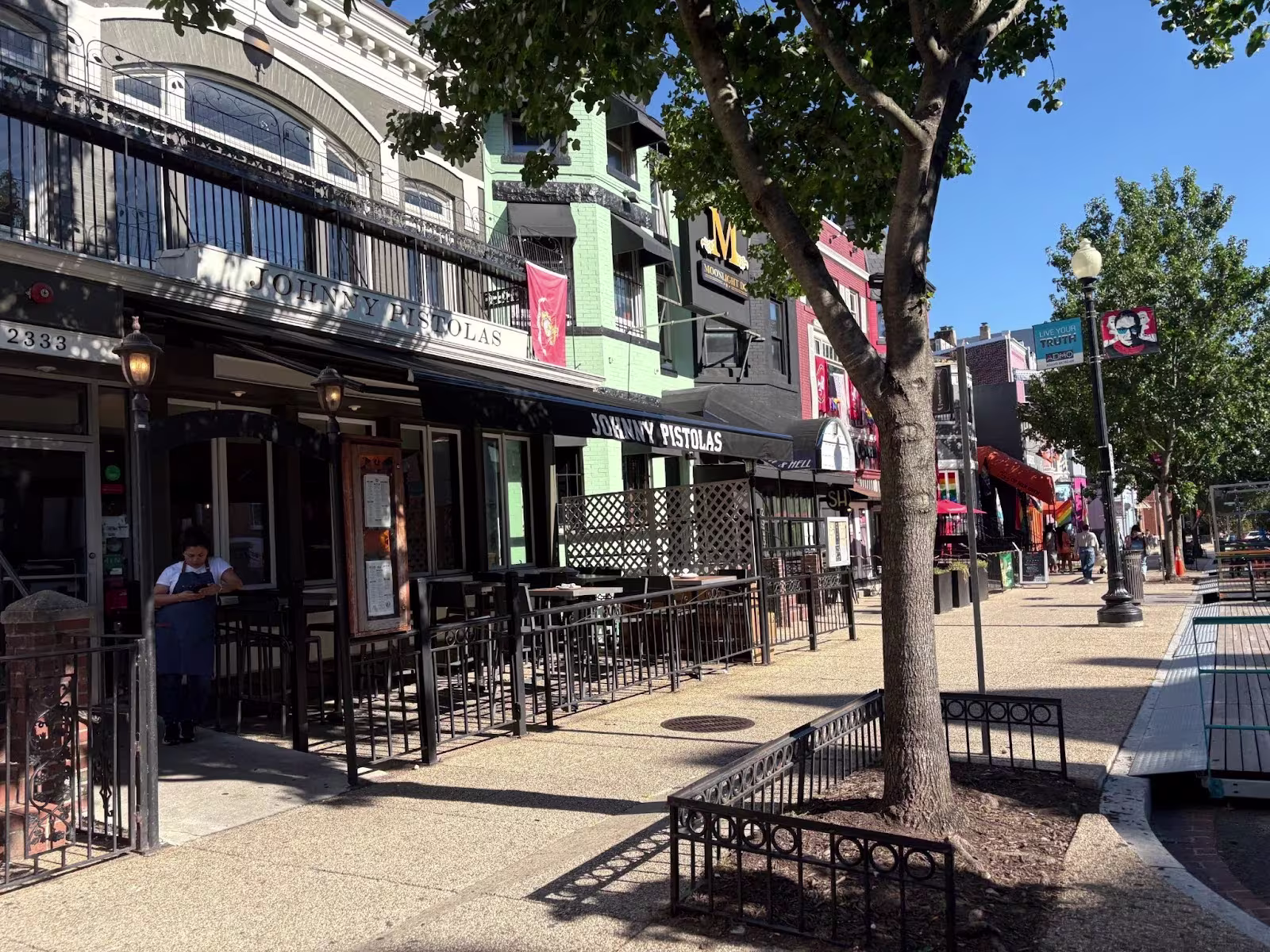 A sidewalk view of a street with shops and restaurants. 
