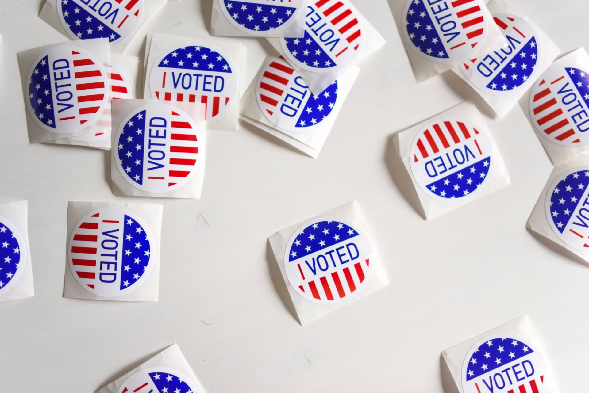 Multiple red, white, and blue "I Voted" stickers are scattered on a white table.