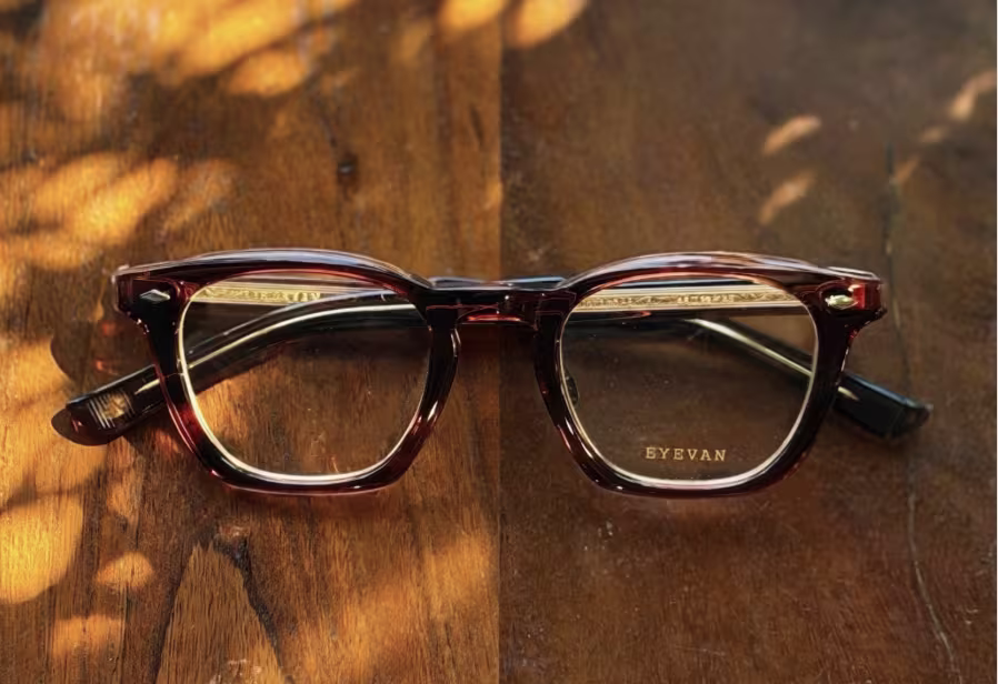  A pair of glasses with brown frames rests on a brown wooden table.