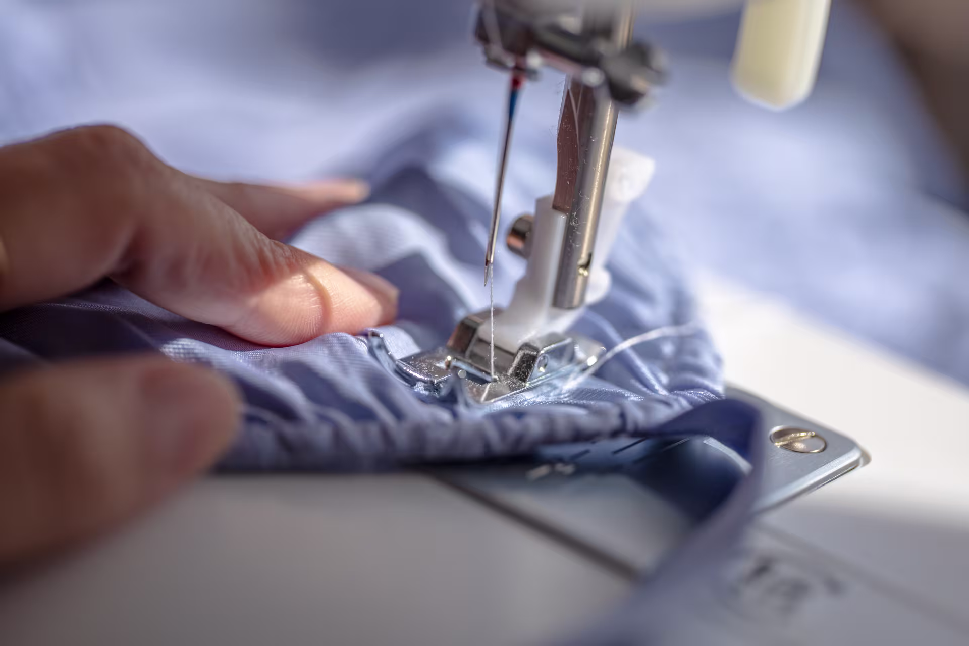 A close-up of hands guiding light blue striped fabric under the needle of a sewing machine.