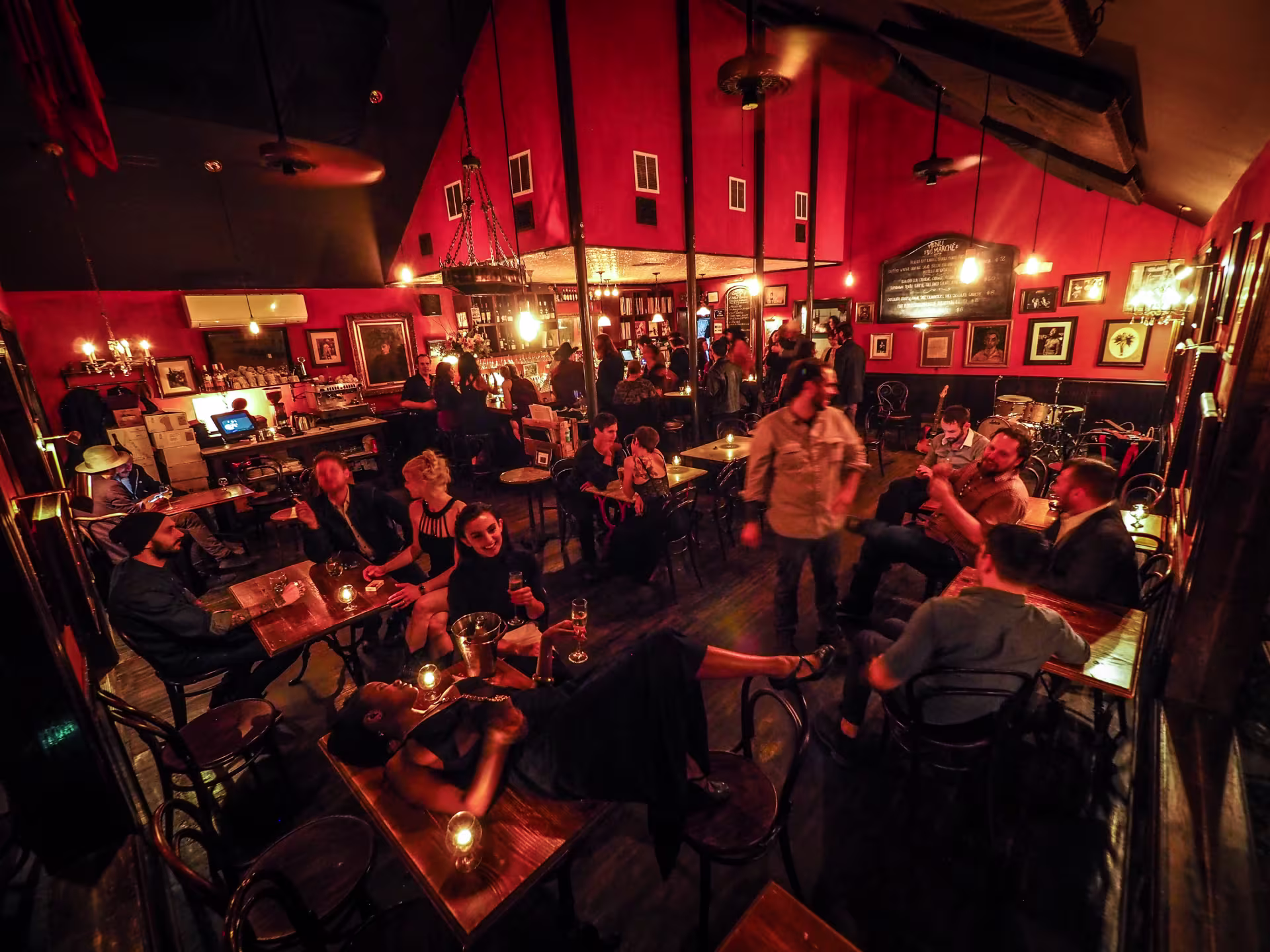 A dark restaurant with red walls and lots of patrons.