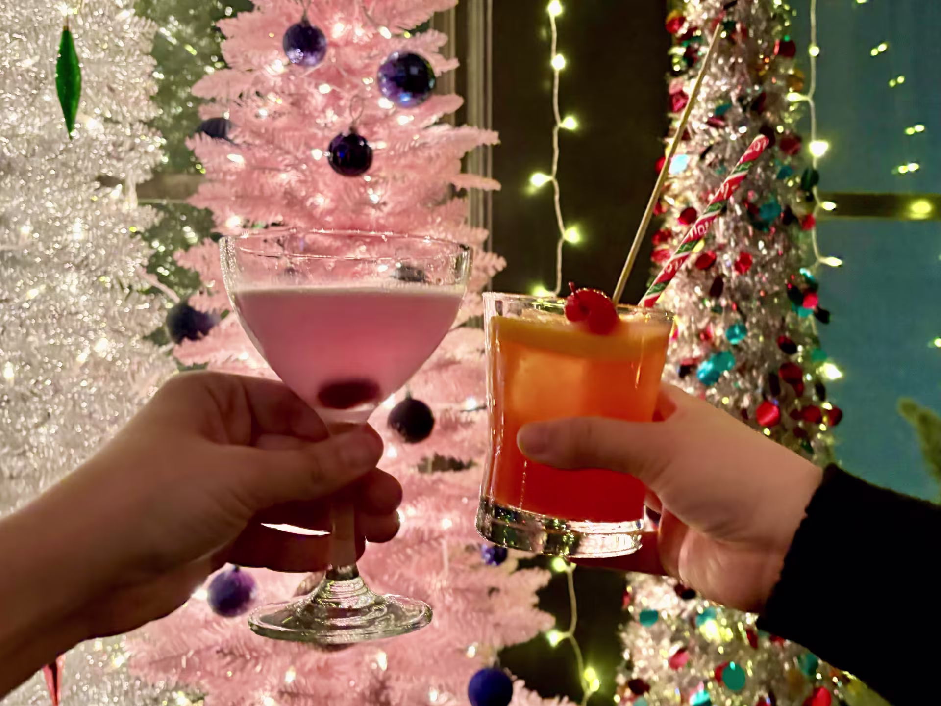 cheers with cocktails in front of holiday trees