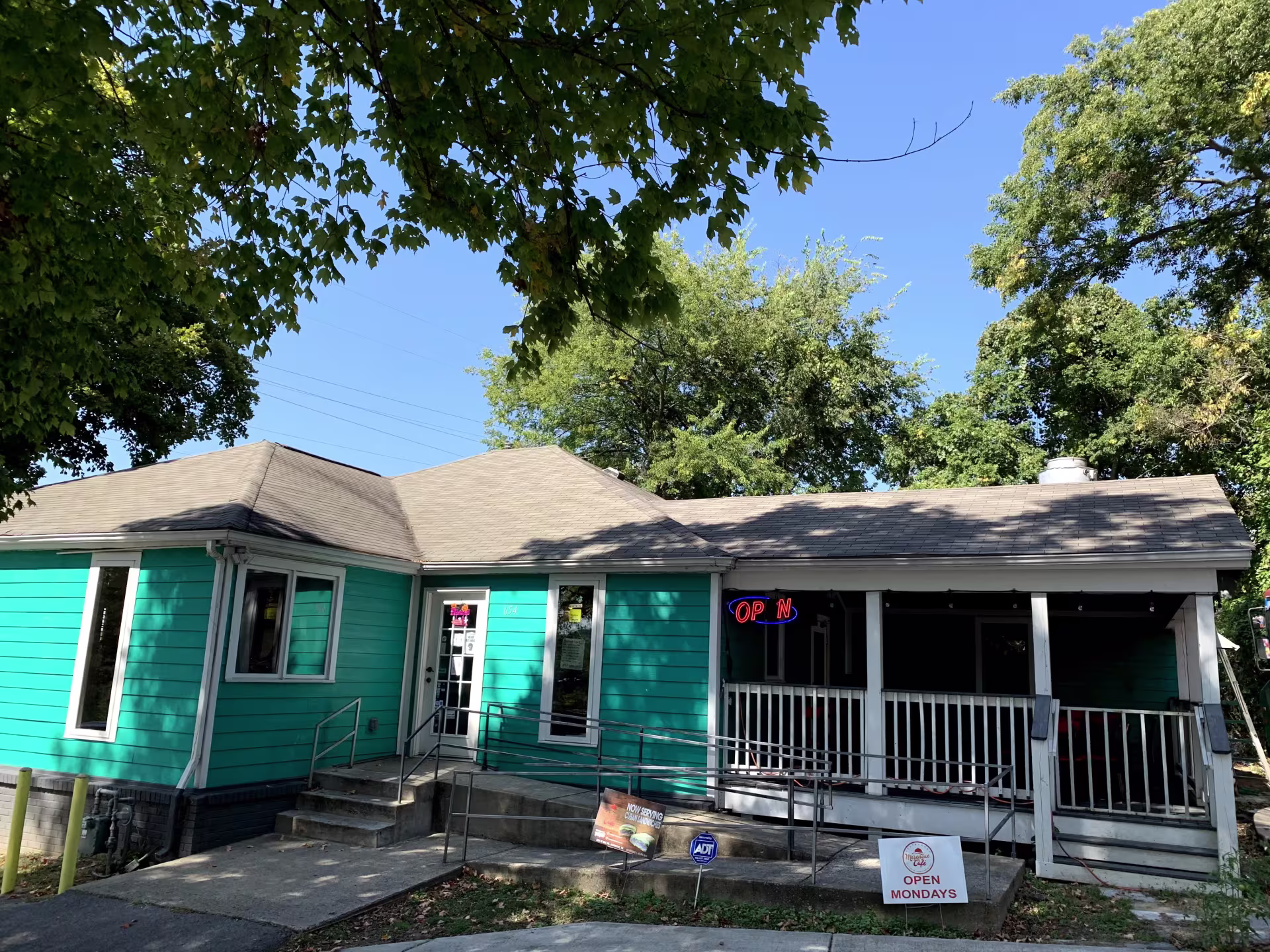 A turquoise home with an open sign surrounded by trees.