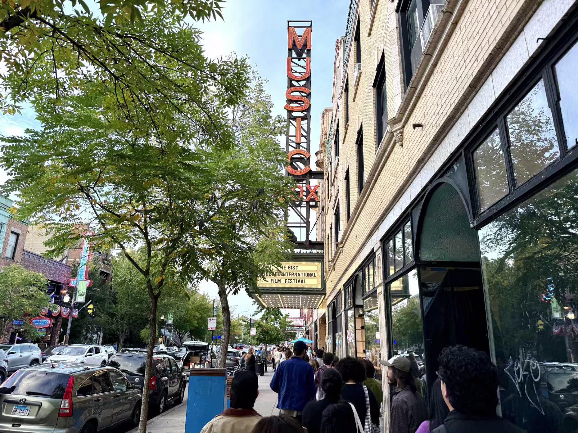 A crowd lines the sidewalk outside the Music Box Theatre in Chicago, where the marquee advertises the 61st Chicago International Film Festival beneath the theater’s iconic vertical neon sign.