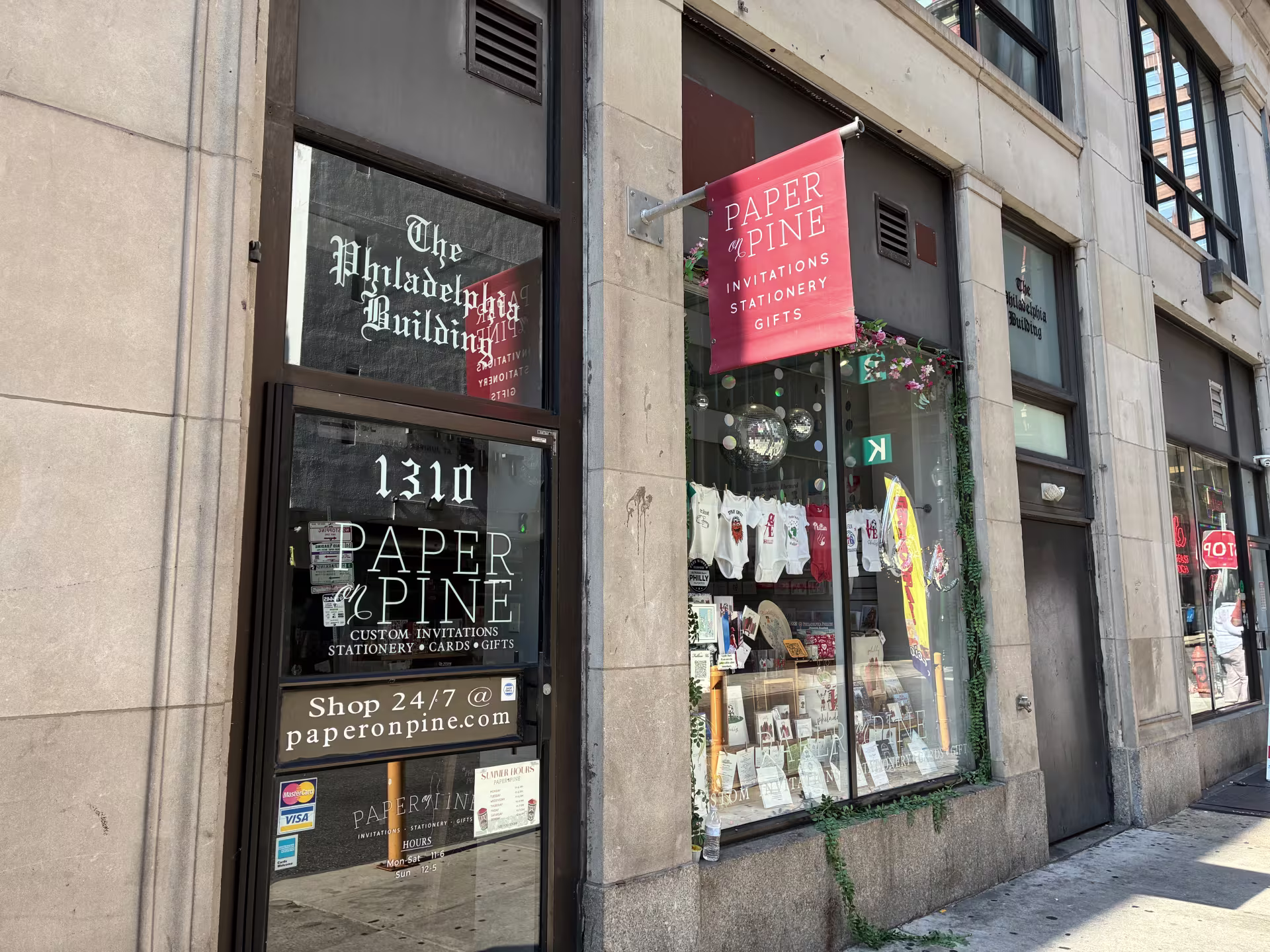The Paper on Pine storefront showing a window display of Philadelphia-themed cards, art, and baby onesies. 