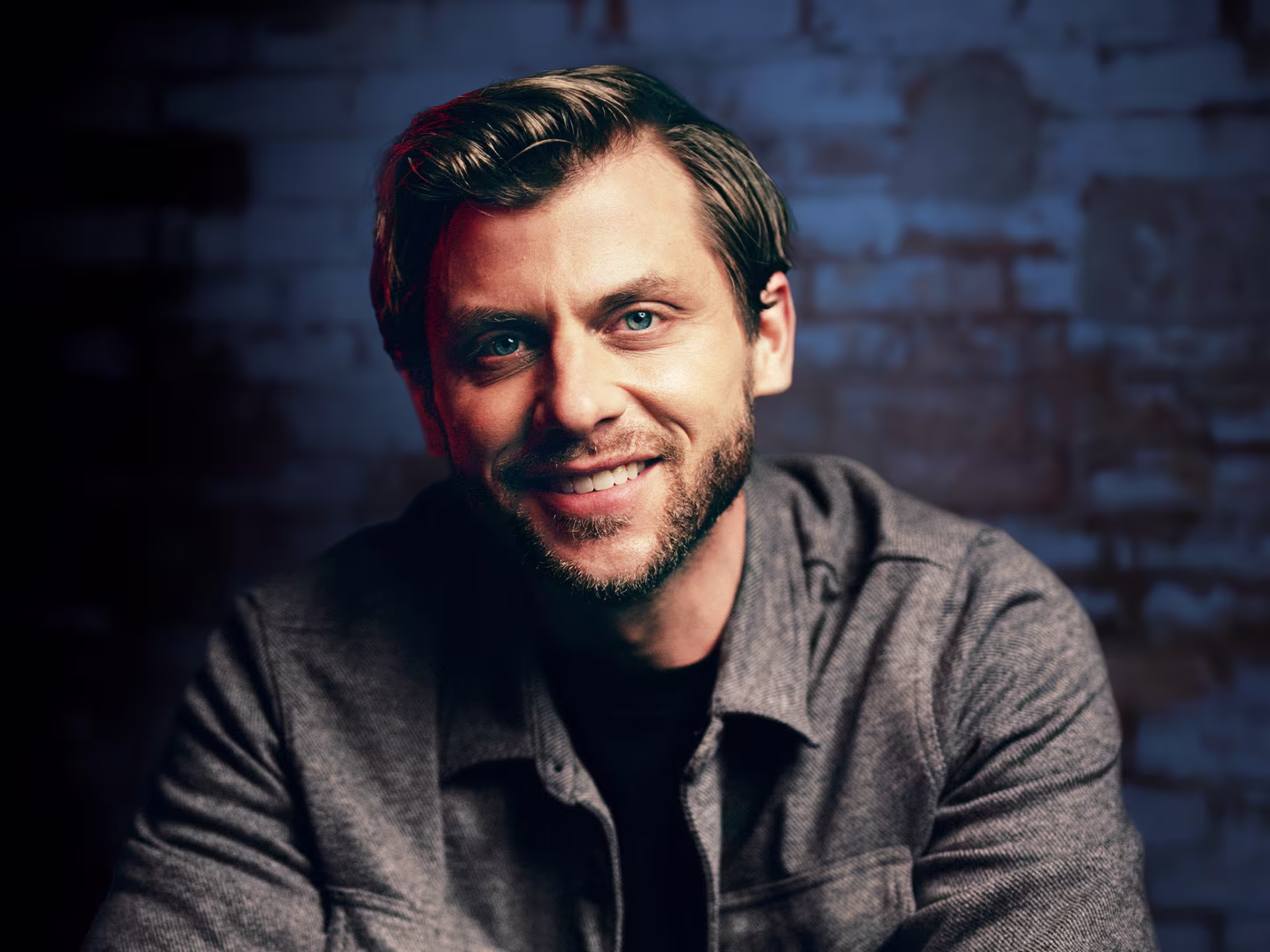 A man in a gray shirt in front of a blue brick wall.