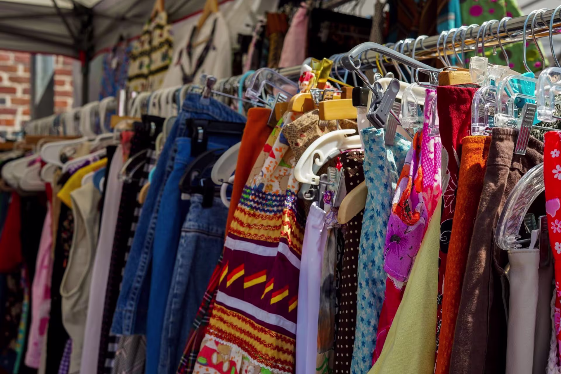 A colorful array of clothes on hangers at a bustling outdoor market.