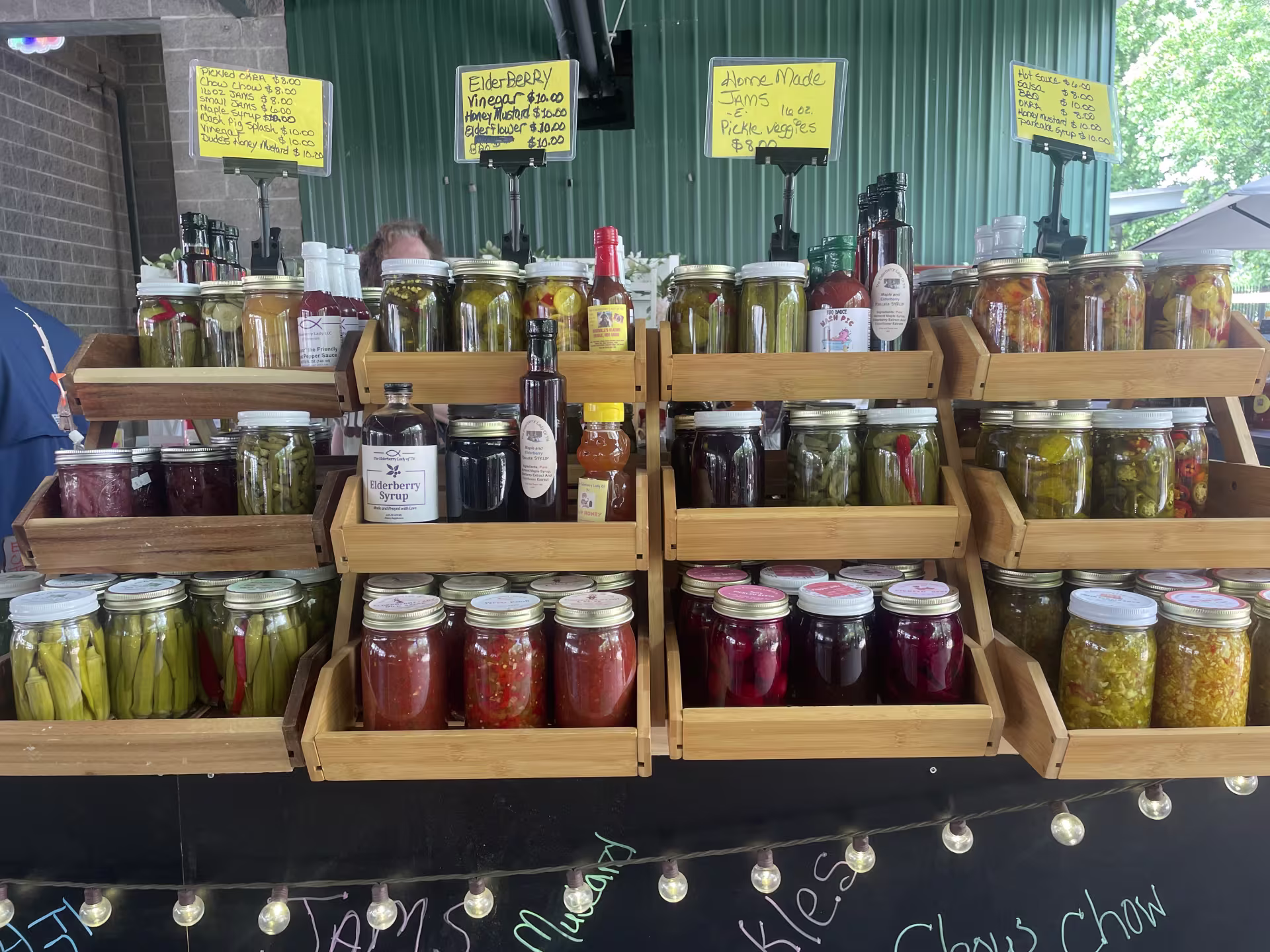 Glass jars full of brightly colored fruits and veggies sit on wooden shelves at an outdoor farmers market shed.