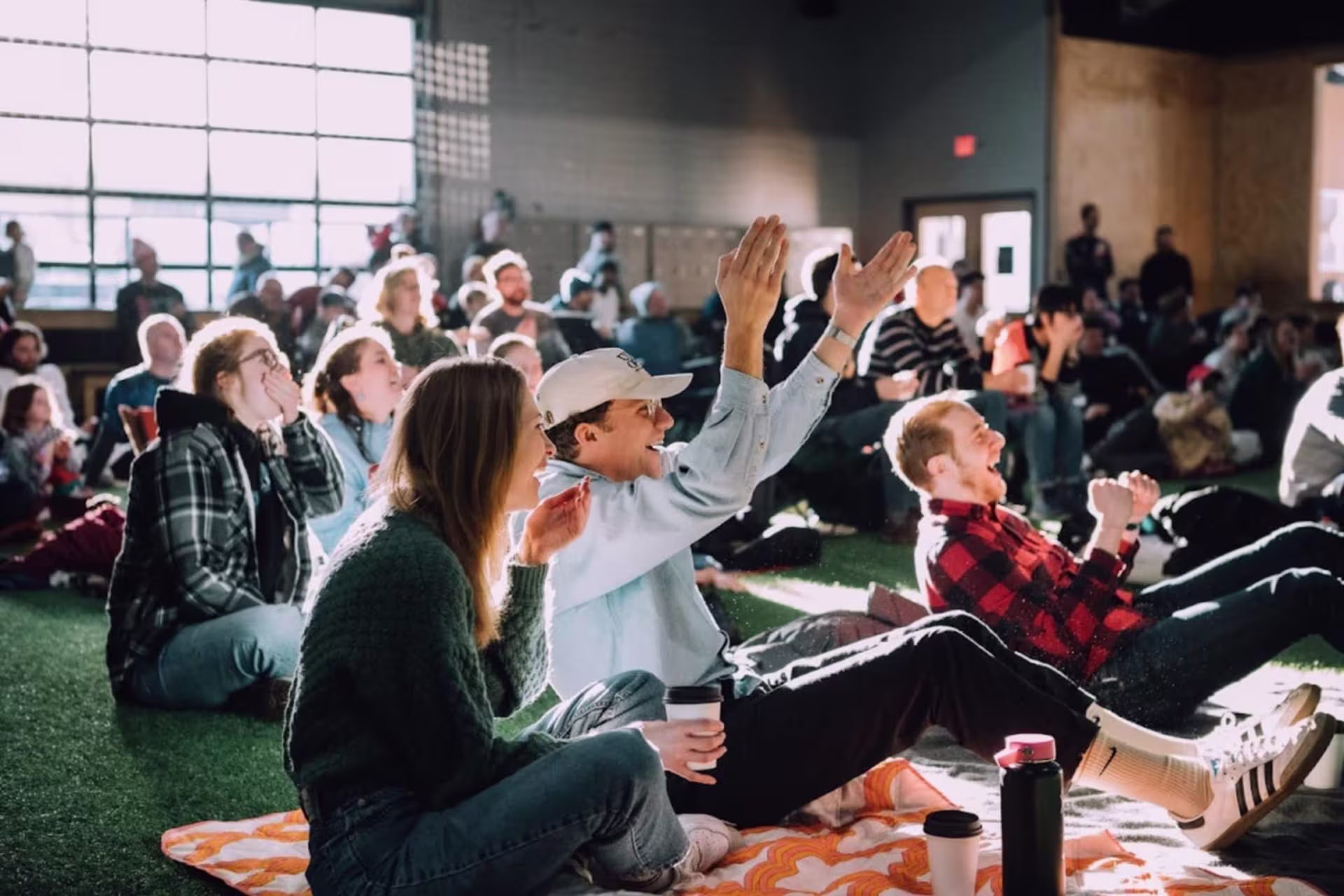 Group of people seated on the ground indoors cheering and all looking the same direction